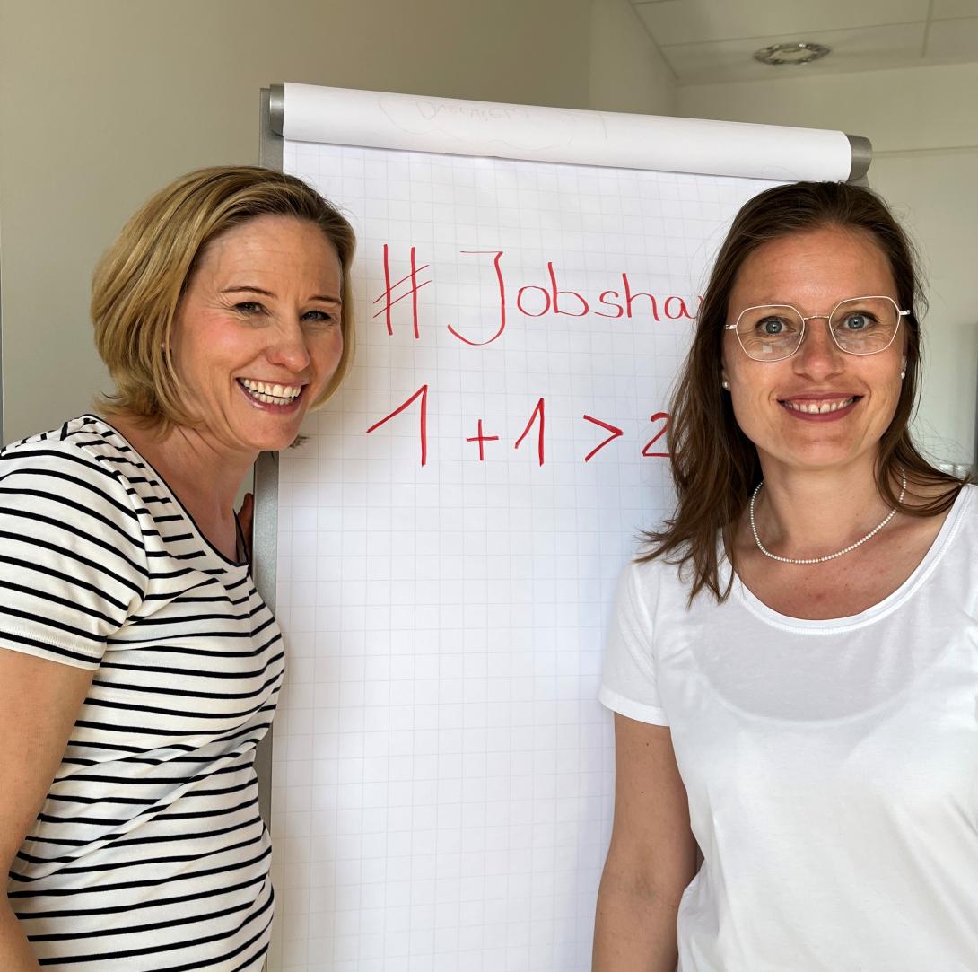 Zwei Frauen stehen lachend vor Flipchart